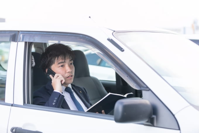 社用車の運転席でノートを片手に携帯で電話をする高沢産業・OAシステム事業部の市川さん